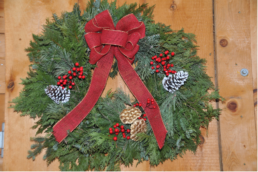A large green wreath is decorated with red berries and pinecones. A large red ribbon, in a bow, hangs from the centre of the wreath.