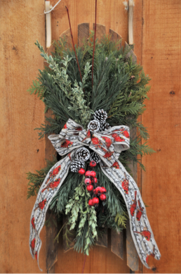 A large sleigh is decorated with evergreen cuttings and red berries. A silver ribbon with red birds, in a bow, is in the centre.
