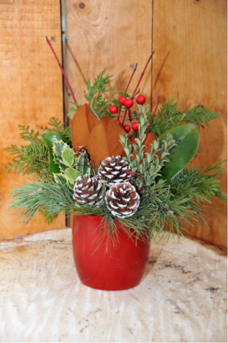 A red vase is filled with evergreen cuttings, red berries, and pinecones.